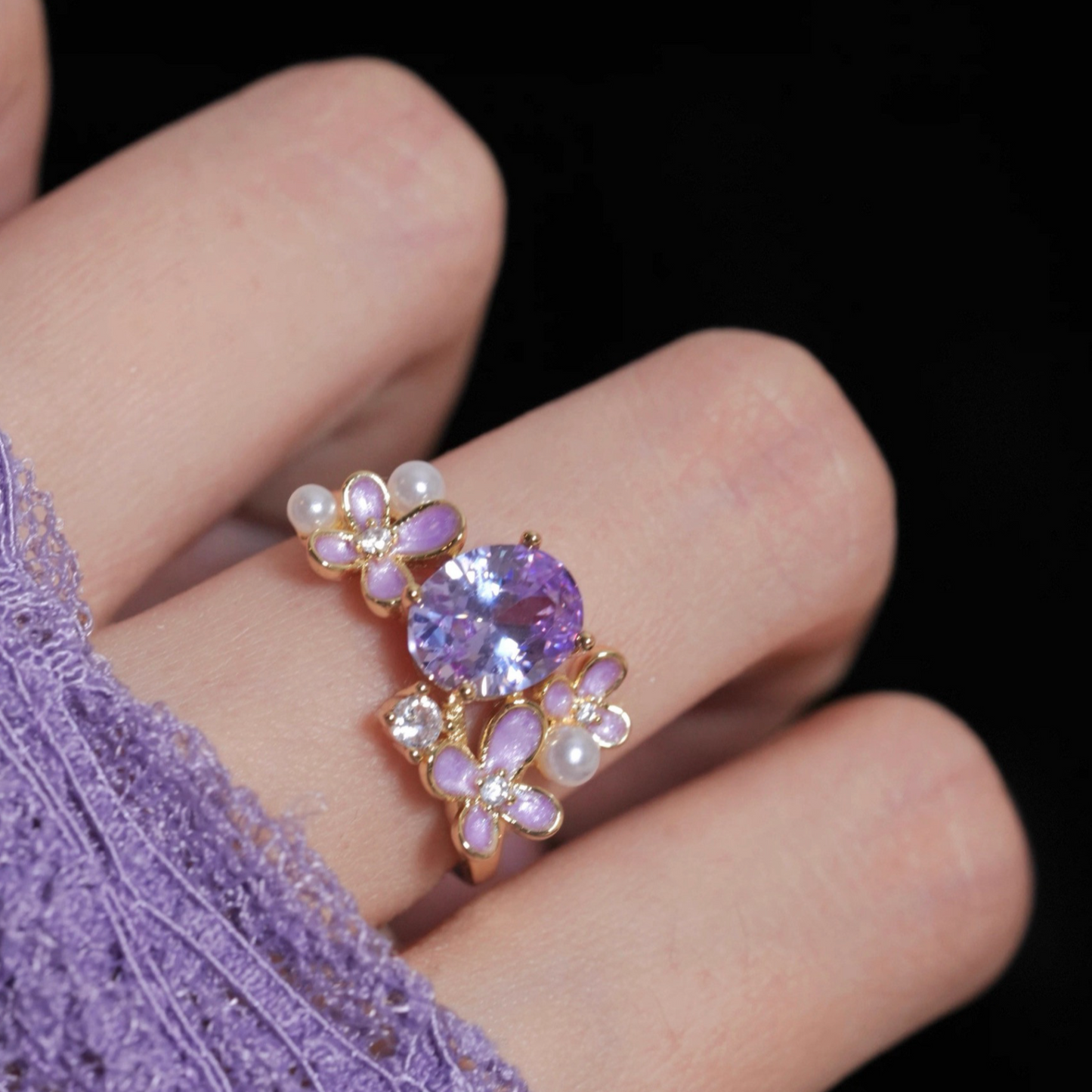Ring with purple gemstone and floral design on a finger against a dark background