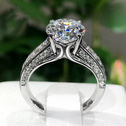 Silver ring with a large diamond and smaller diamonds on the band against a blurred green background