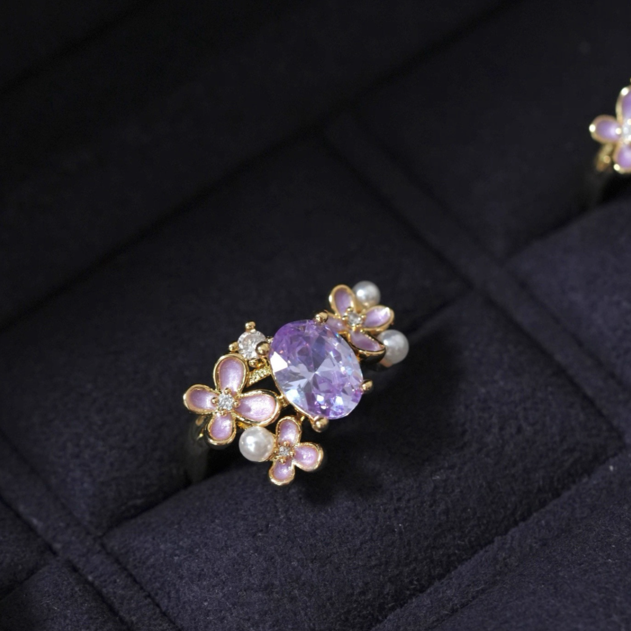 Gold ring with a purple gemstone and floral design on a dark fabric background