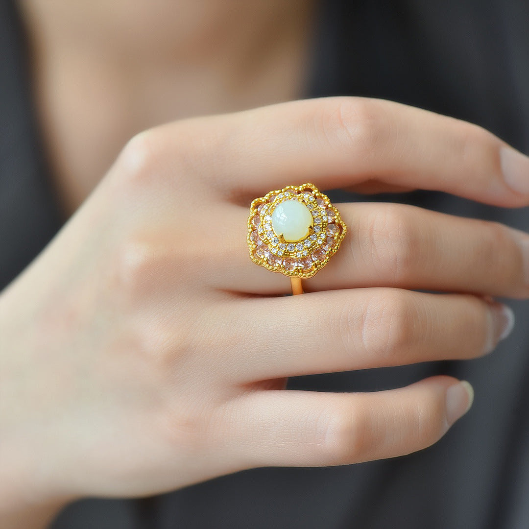 Gold ring with a central gemstone on a person's finger against a neutral background