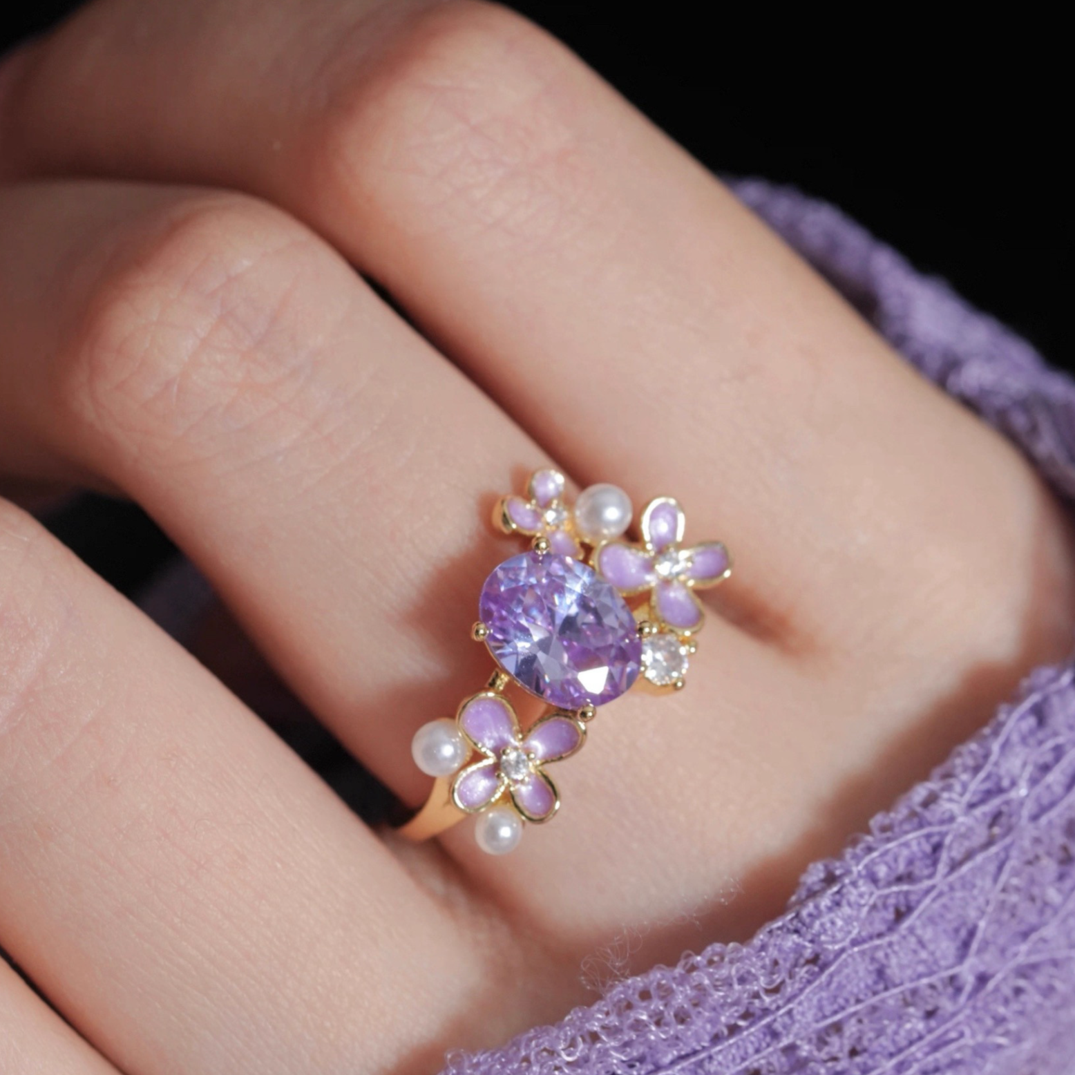 Close-up of a hand wearing a decorative ring with purple gemstone and pearls.