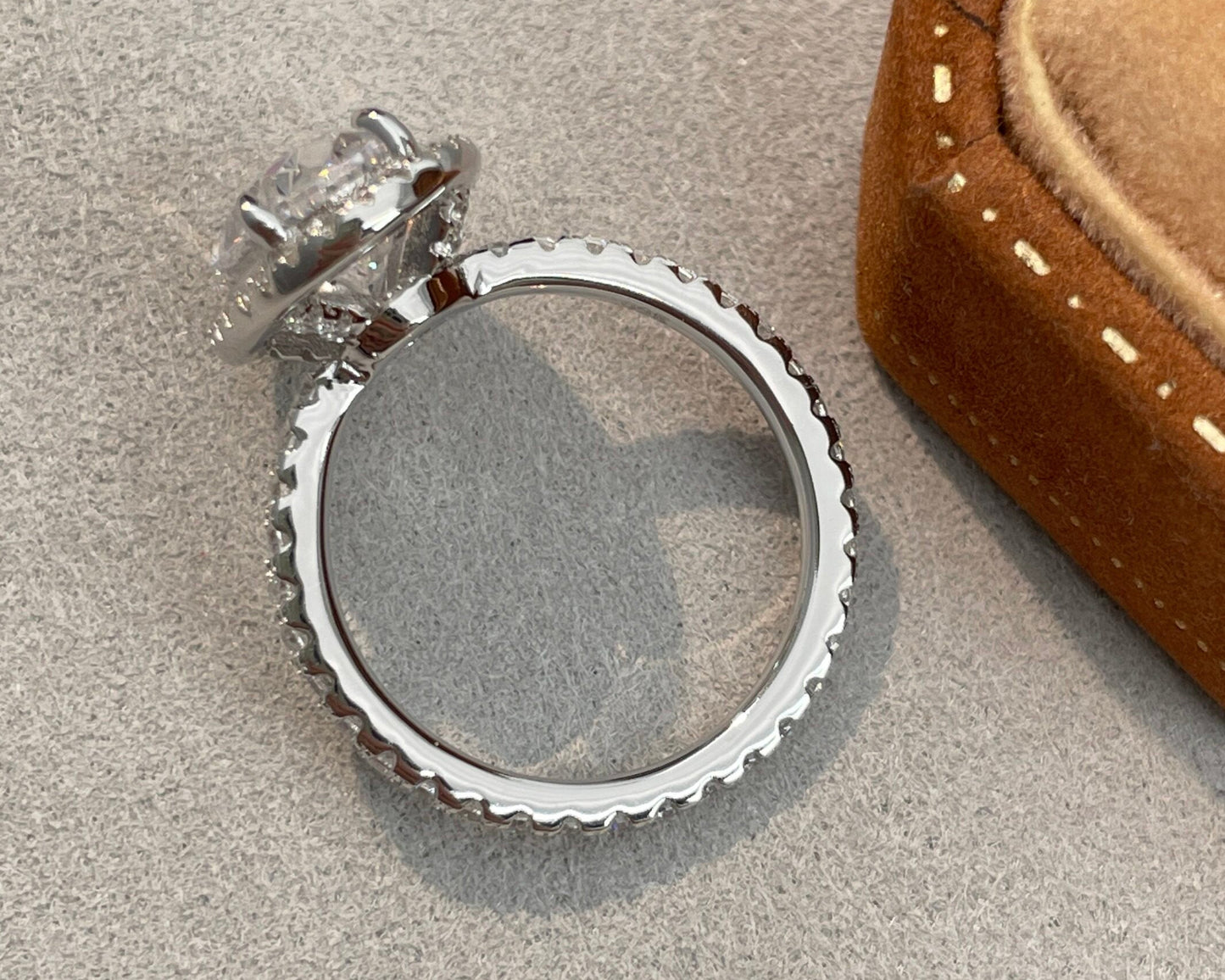 Silver ring with a textured band on a textured surface next to a brown jewelry box.